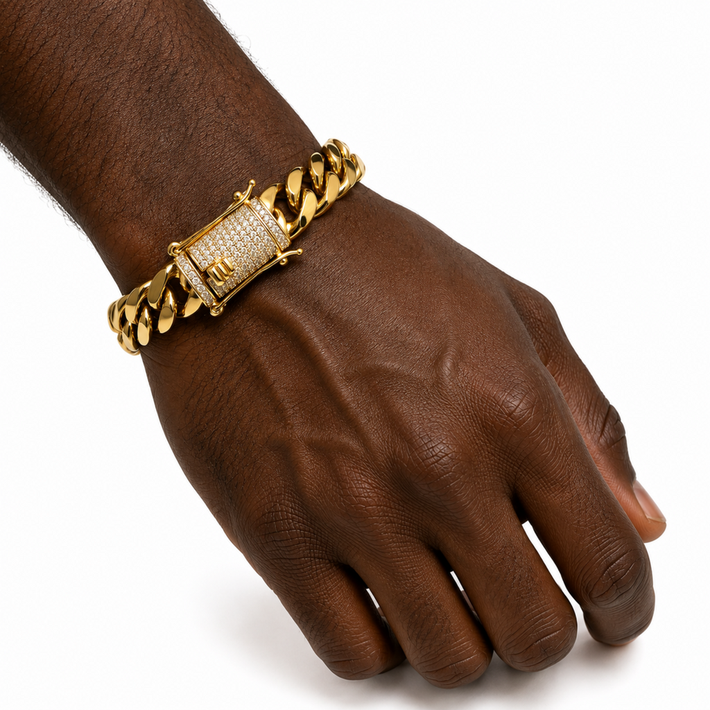 A gold-toned Cuban link chain bracelet with a rectangular clasp paved with clear stones and featuring a small gold 'H' emblem, shown worn on a person's wrist against a white background.