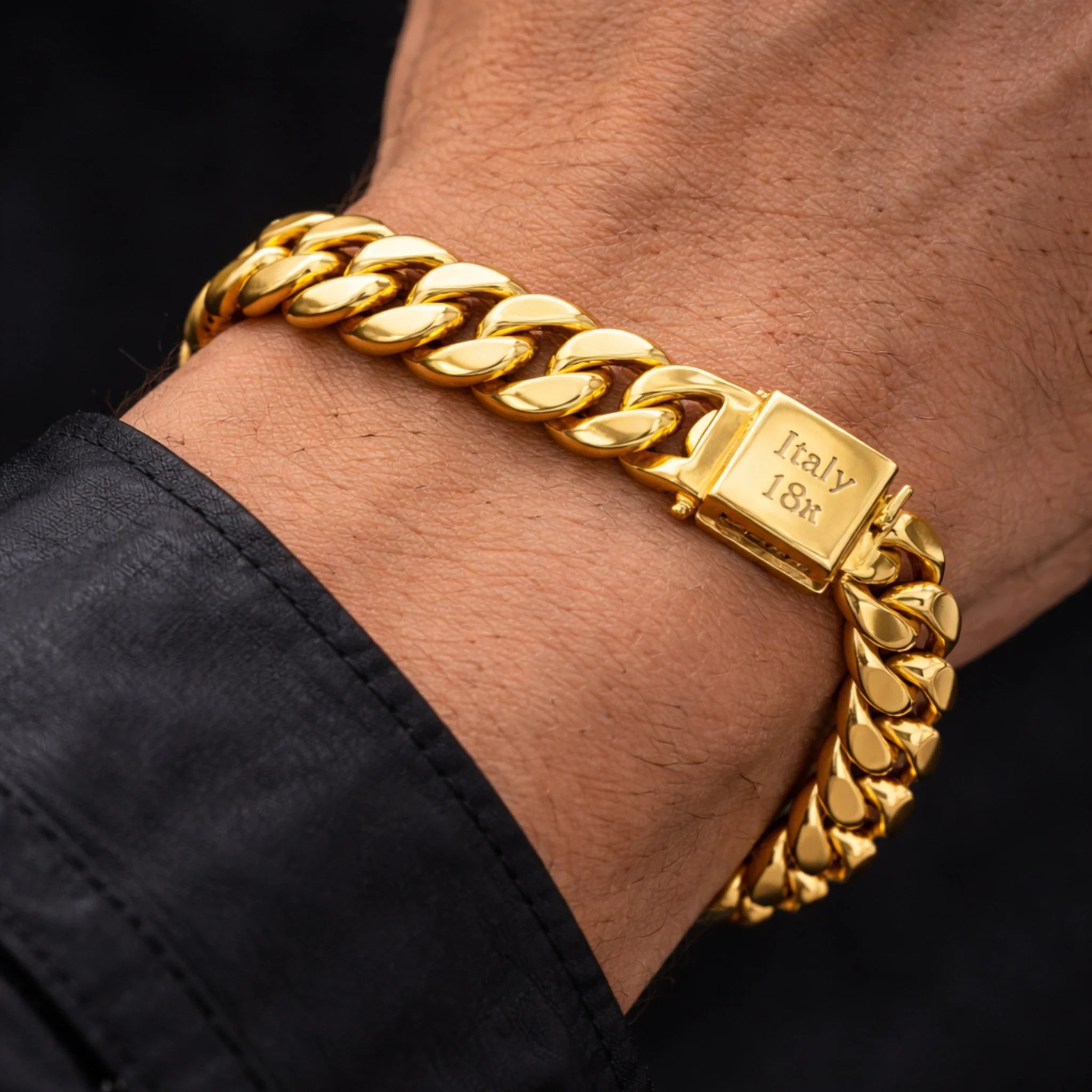 Gold chain bracelet on a wrist with 'Italy 18k' stamp, against a black background.